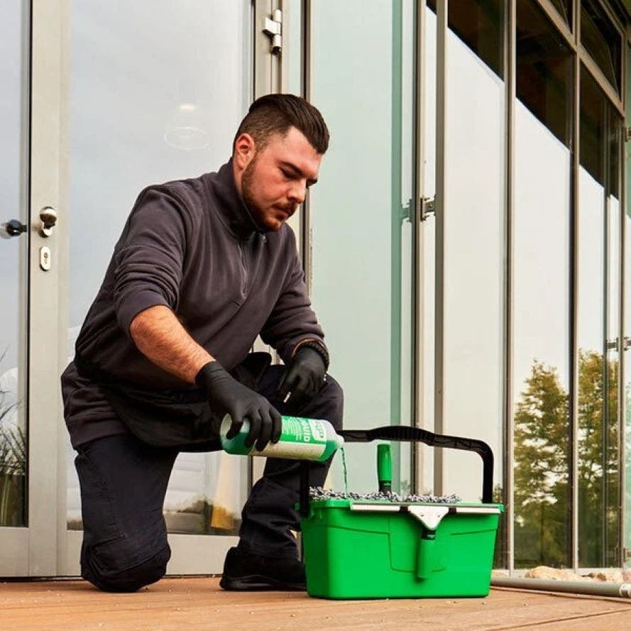Glazenwasser vult emmer met glasreinigingsmiddel van glazenwasserset