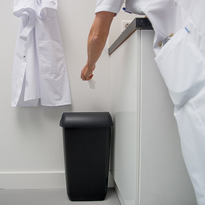 Persoon gooit afval weg in sanitaire afvalbak - Afvalbak op toilet